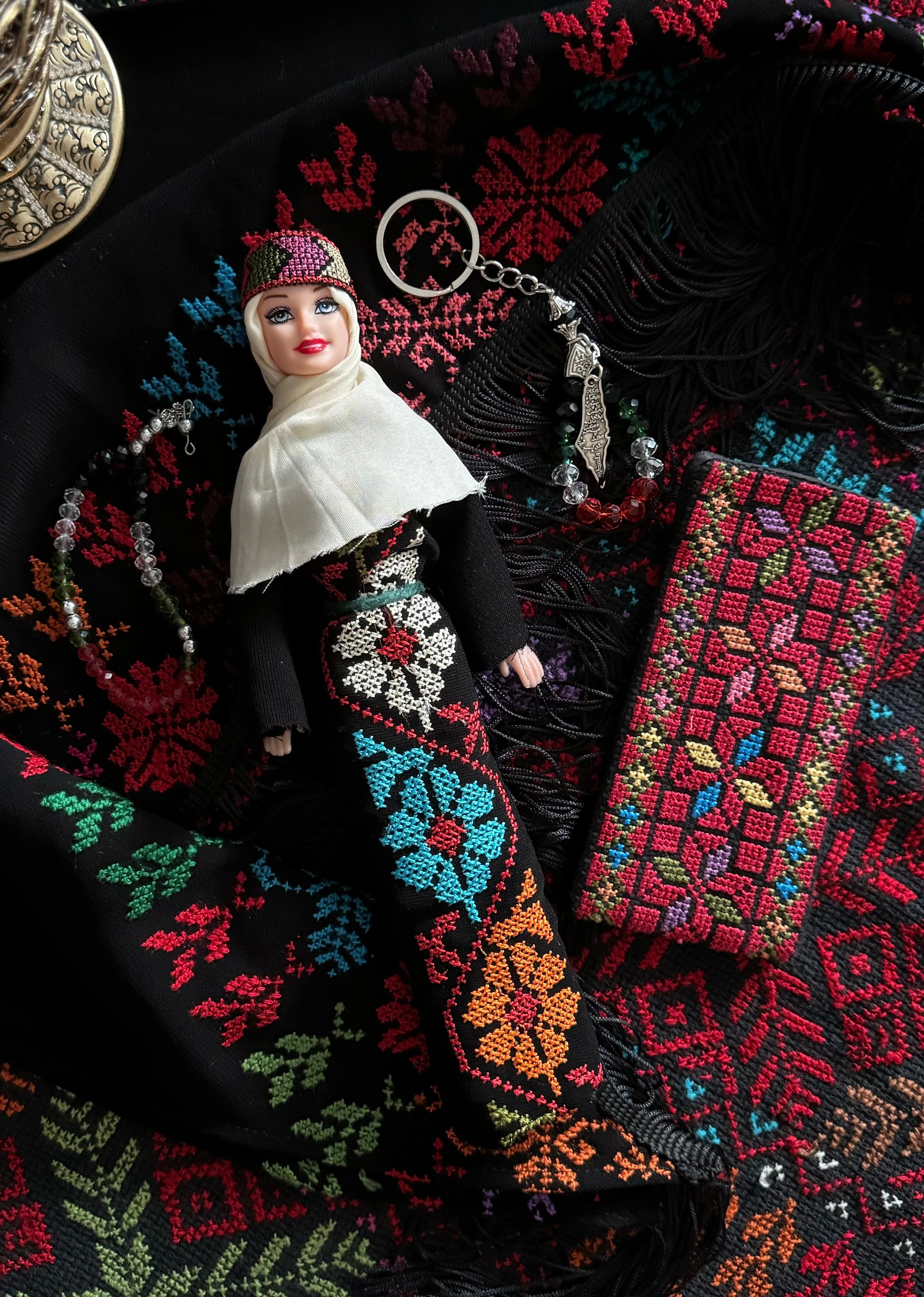 Tatreez-dukke kledd i tradisjonell palestinsk drakt med brodert tatreez-mønster, presentert mot matchende tatreez-tekstil