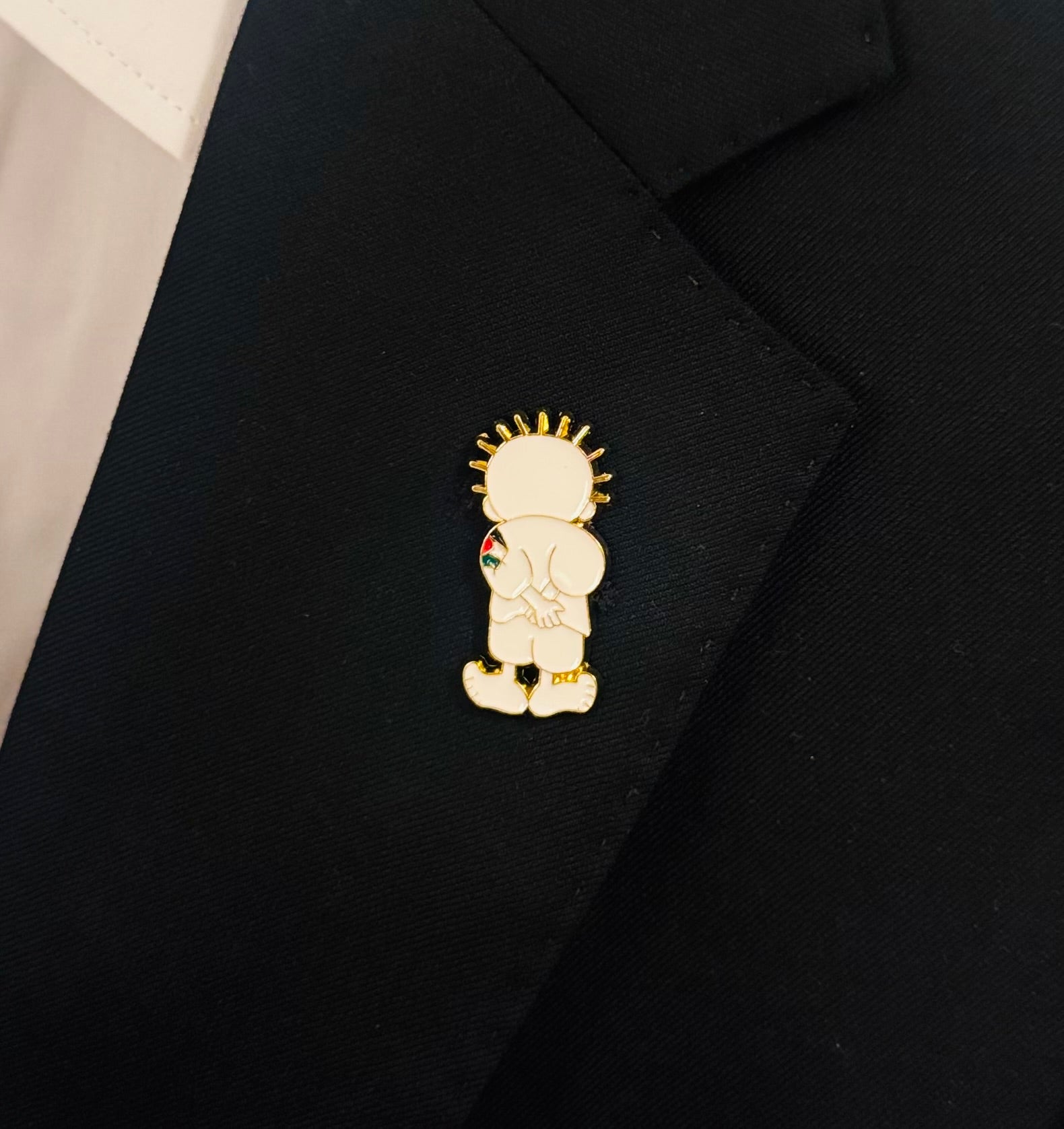 Emaljepin med Handala-figuren, festet på et svart plagg.