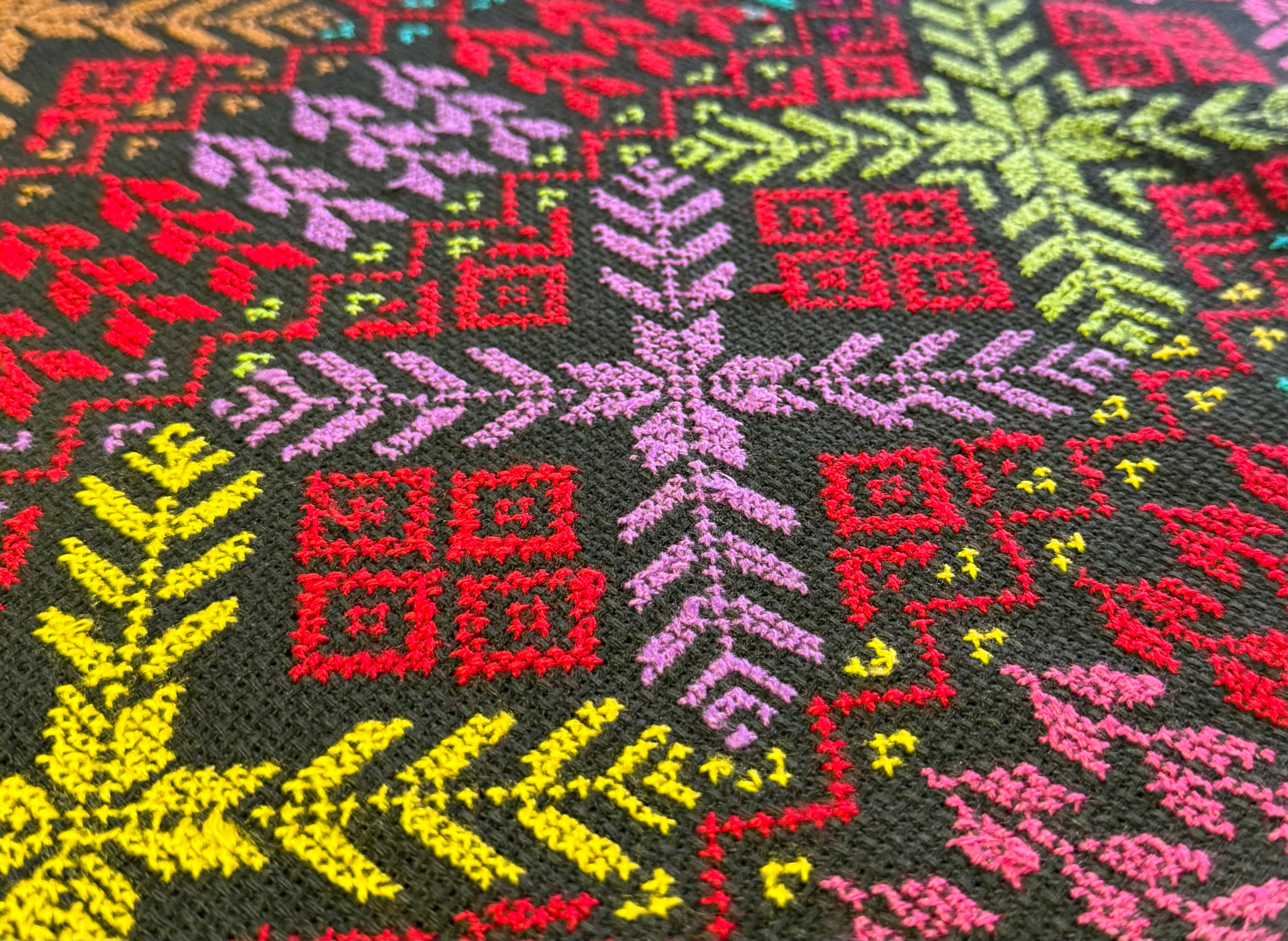 Tatreez-broderi fotografert fra skrå vinkel, der dybde i stingene og tekstur i stoffet fremheves gjennom lys og perspektiv.