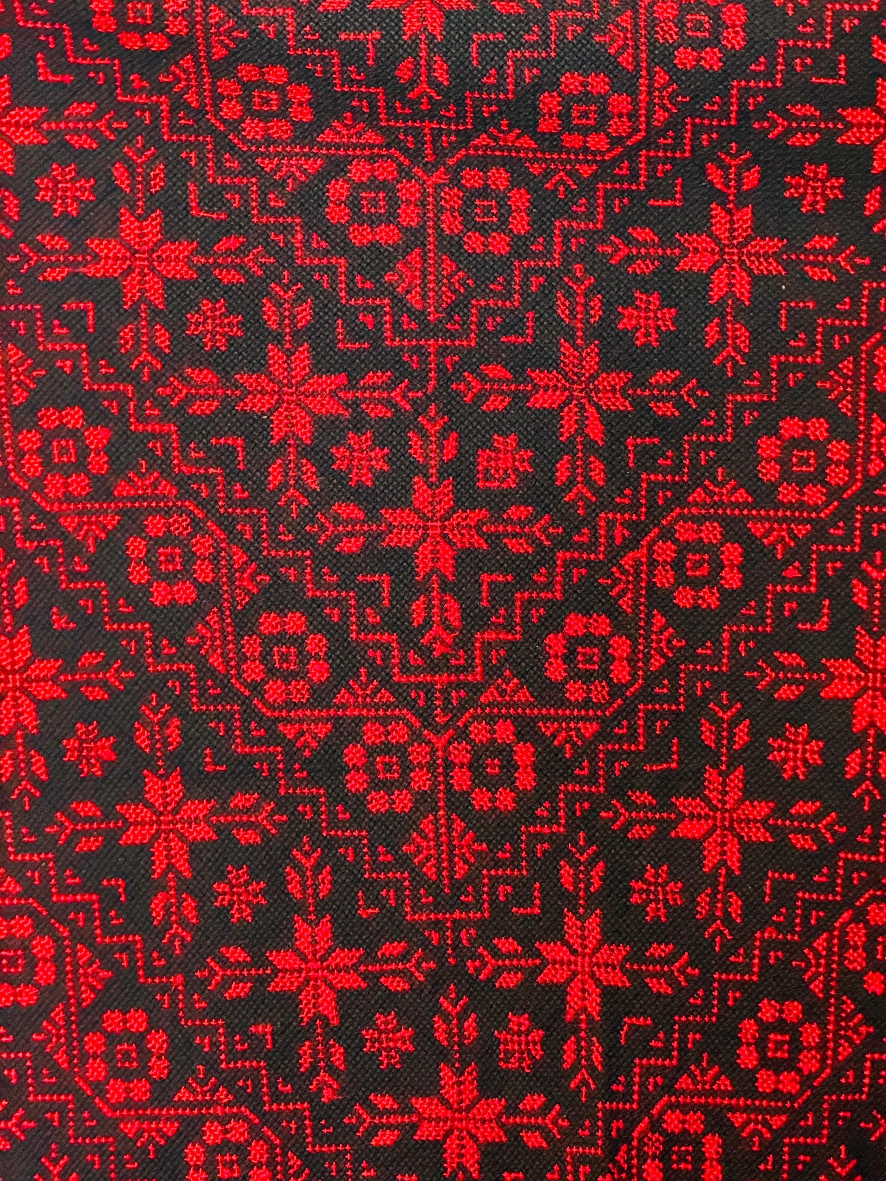 Nærbilde av rødt og svart palestinsk tatreez-broderi med markerte geometriske mønstre og tydelig tekstilstruktur