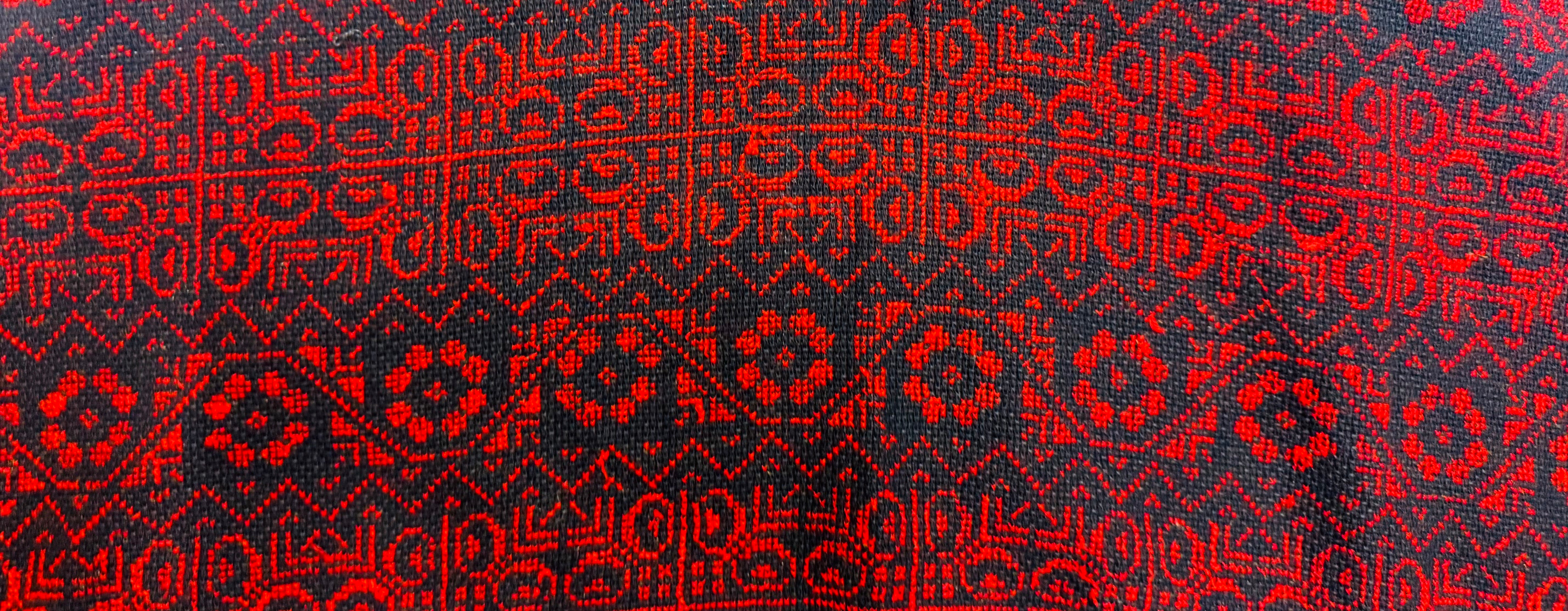 Horisontalt bilde av rødt og svart palestinsk tatreez-mønster med tradisjonelle geometriske detaljer i vevd tekstil