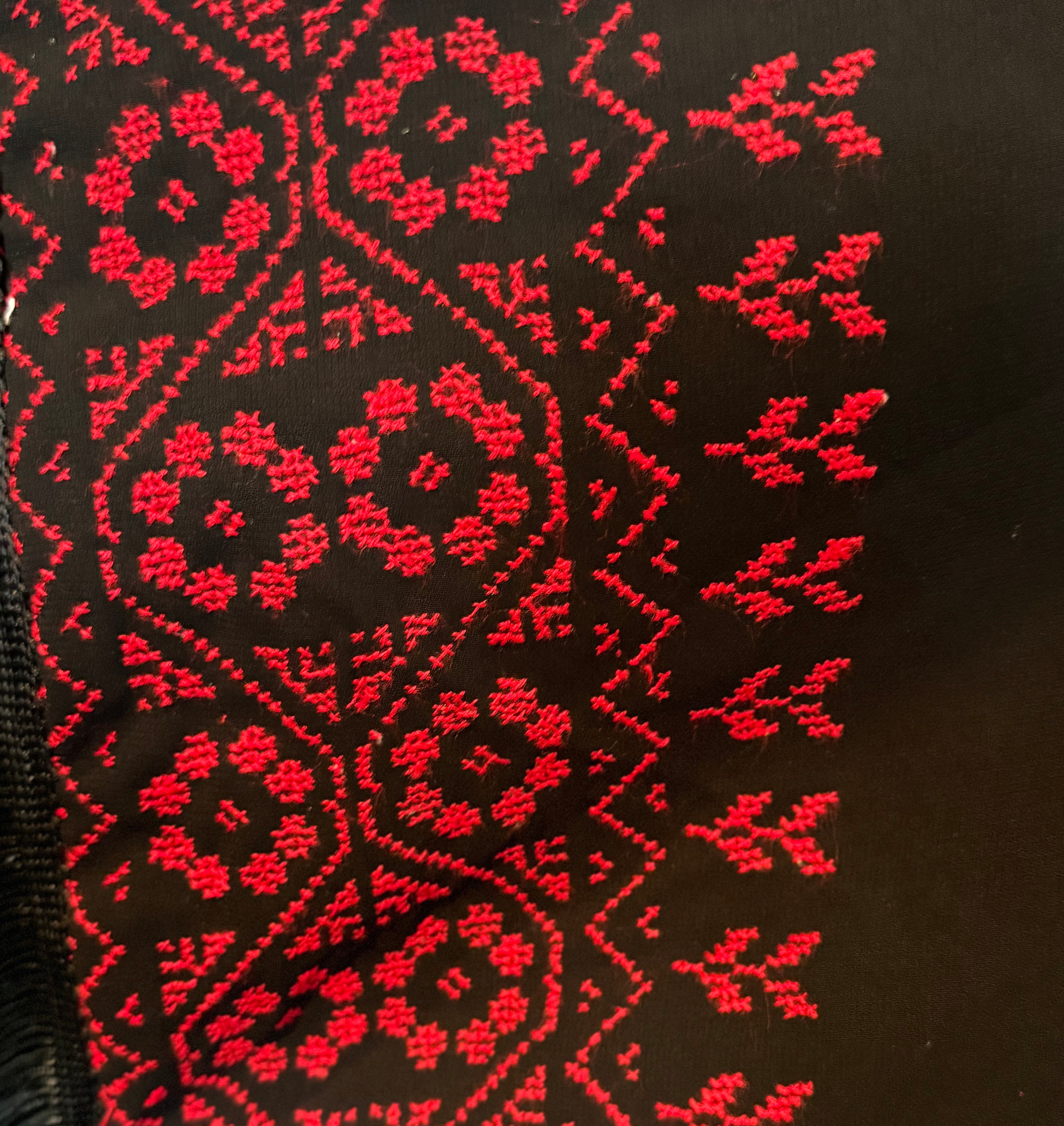 Detaljert tatreez-broderi i rødt, vist på mørkt stoff fra et skjerf.