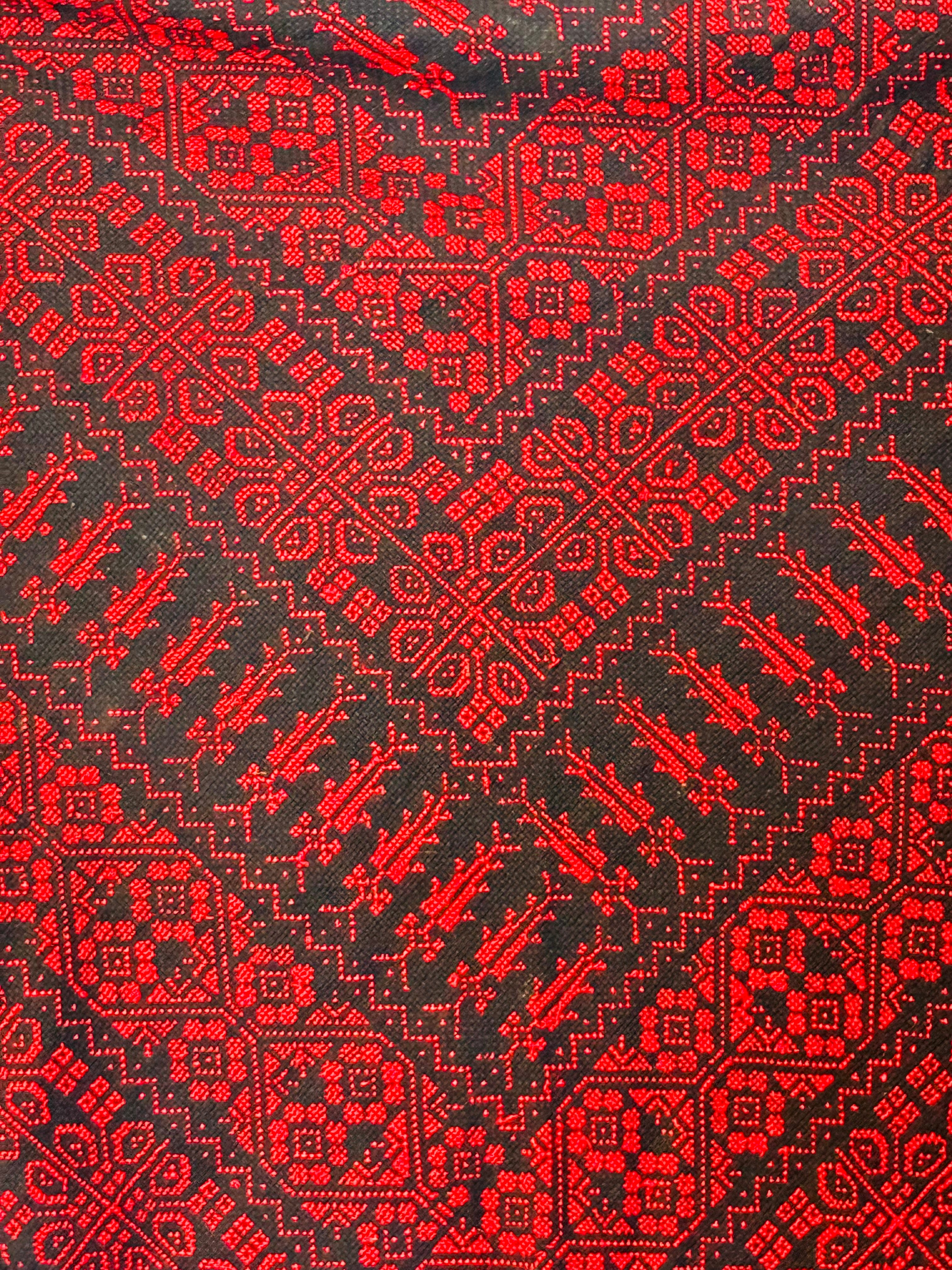 Teksturnært nærbilde av rødt og svart tatreez-mønster, håndbrodert palestinsk design med tydelige detaljer