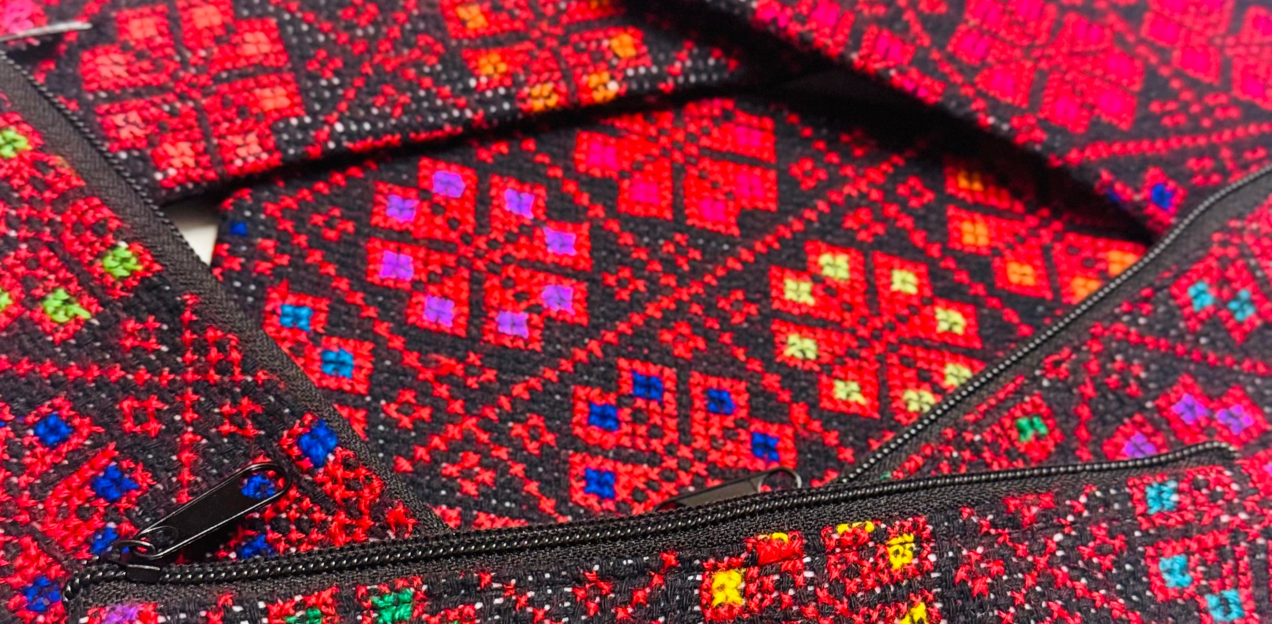 Horisontalt nærbilde av flere tatreez-lommebøker sammen, der broderidetaljene vises i bredt utsnitt.
