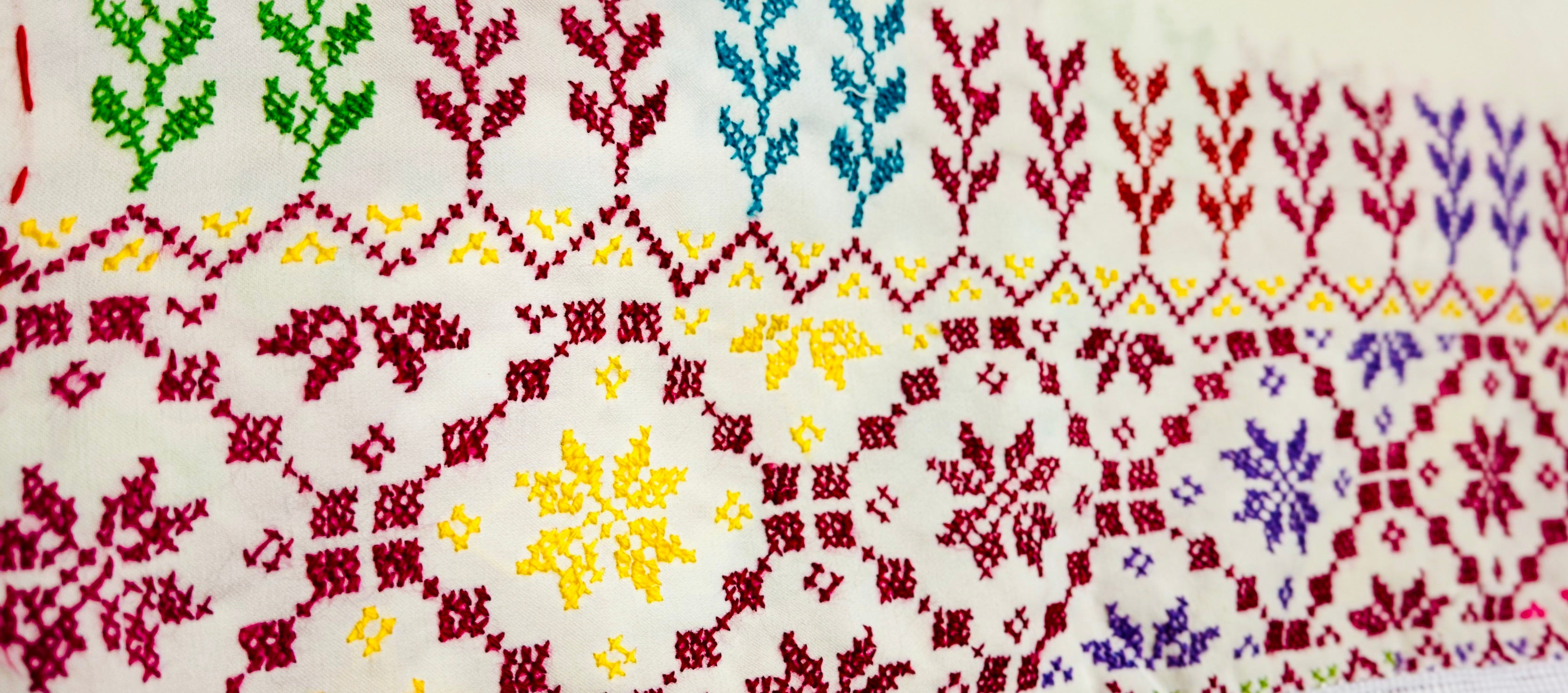 Horisontalt nærbilde av palestinsk tatreez-broderi på hvitt sjal, detaljerte geometriske mønstre i tradisjonelt håndverk