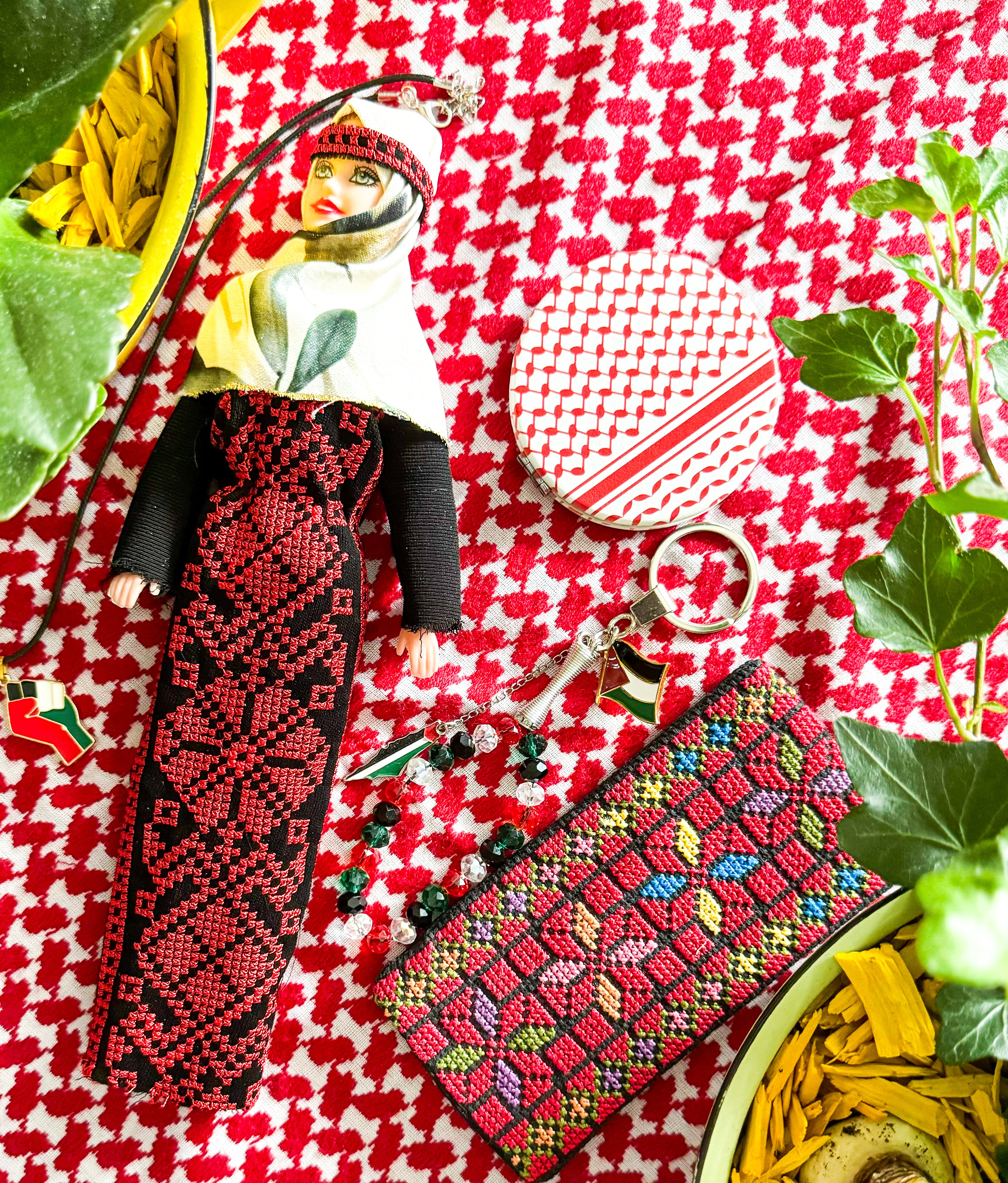 Håndlaget tatreez-dukke fotografert mot en rød kufiyeh, der det klassiske palestinske skjerfmønsteret skaper sterk kontrast og kulturell dybde.