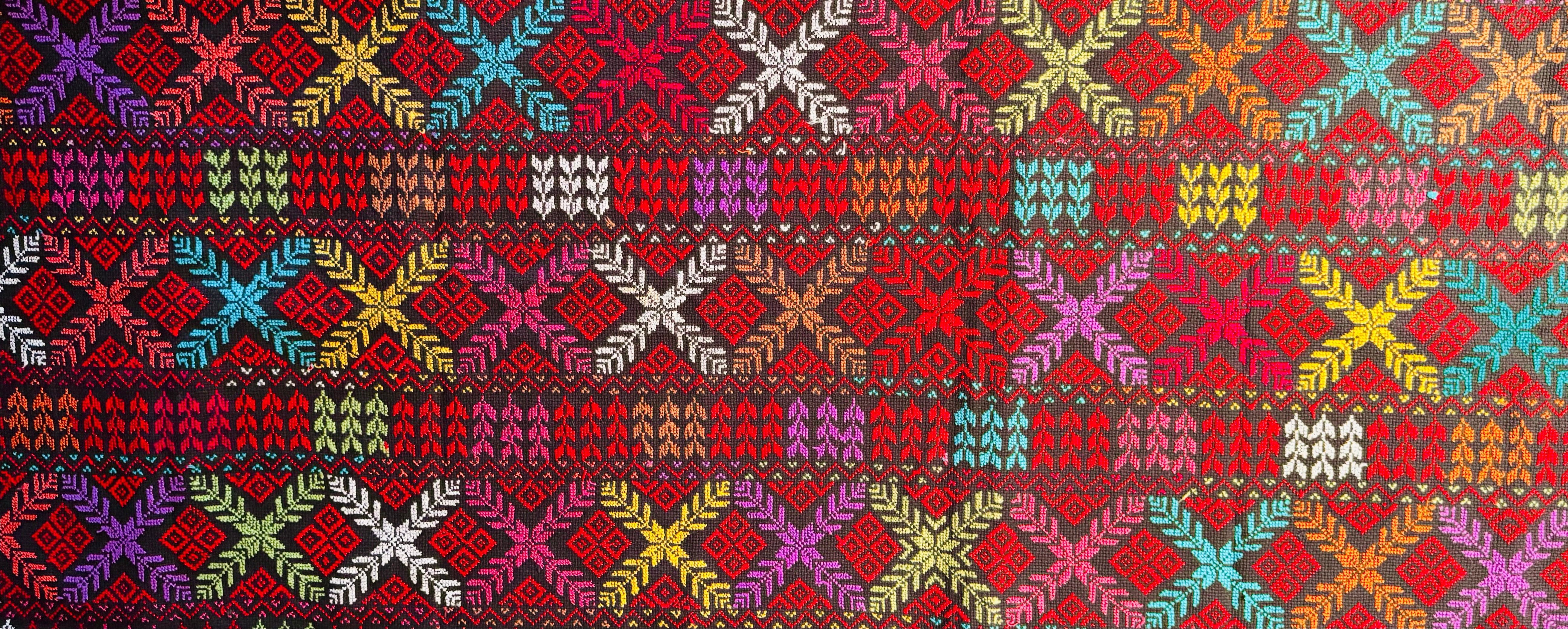 Horisontalt utsnitt av tatreez-tekstil som viser broderte symboler strukket over stoffet, med fokus på mønsterflyt og håndlaget presisjon.