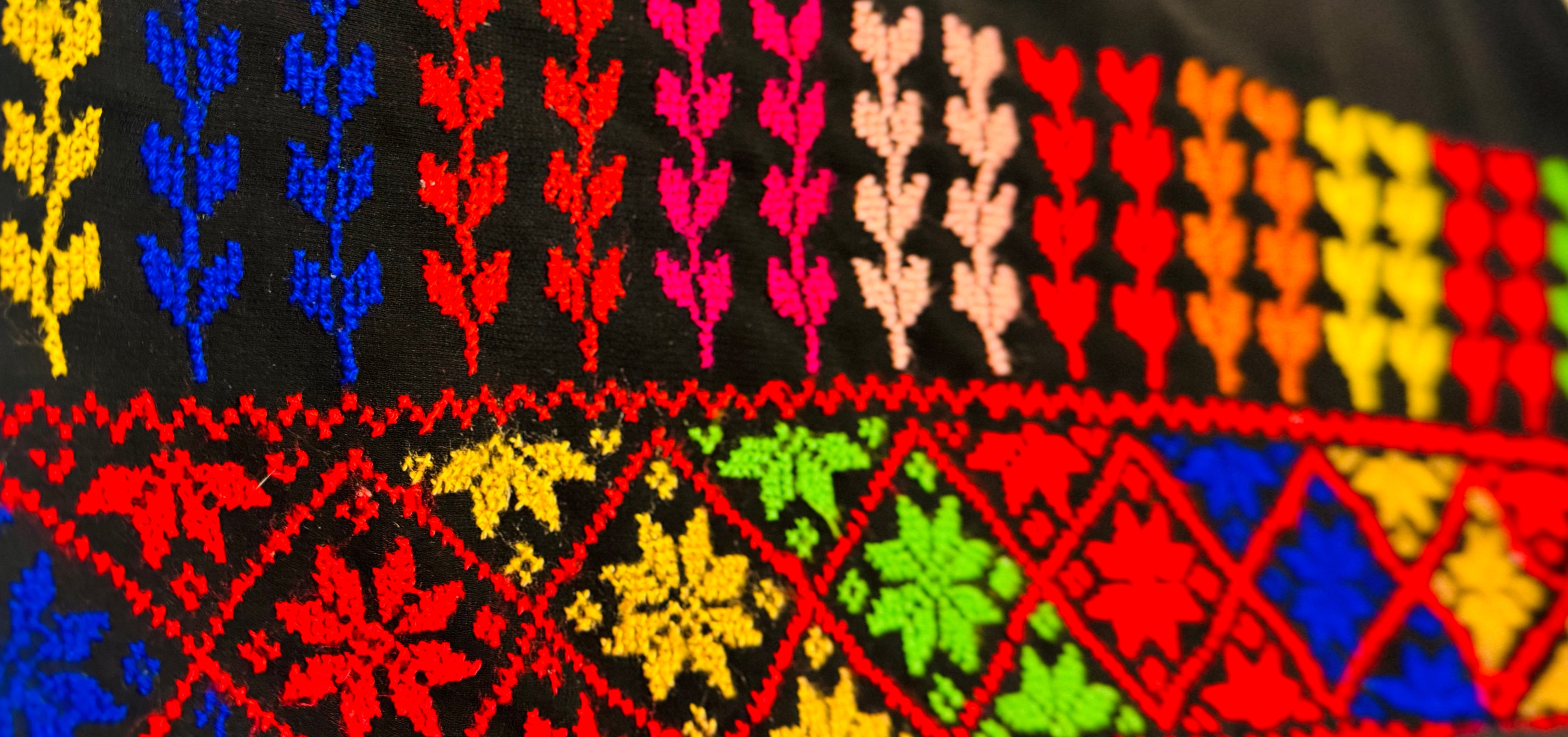 Horisontalt bilde av fargerikt palestinsk tatreez-broderi med detaljerte geometriske mønstre i vevd tekstil