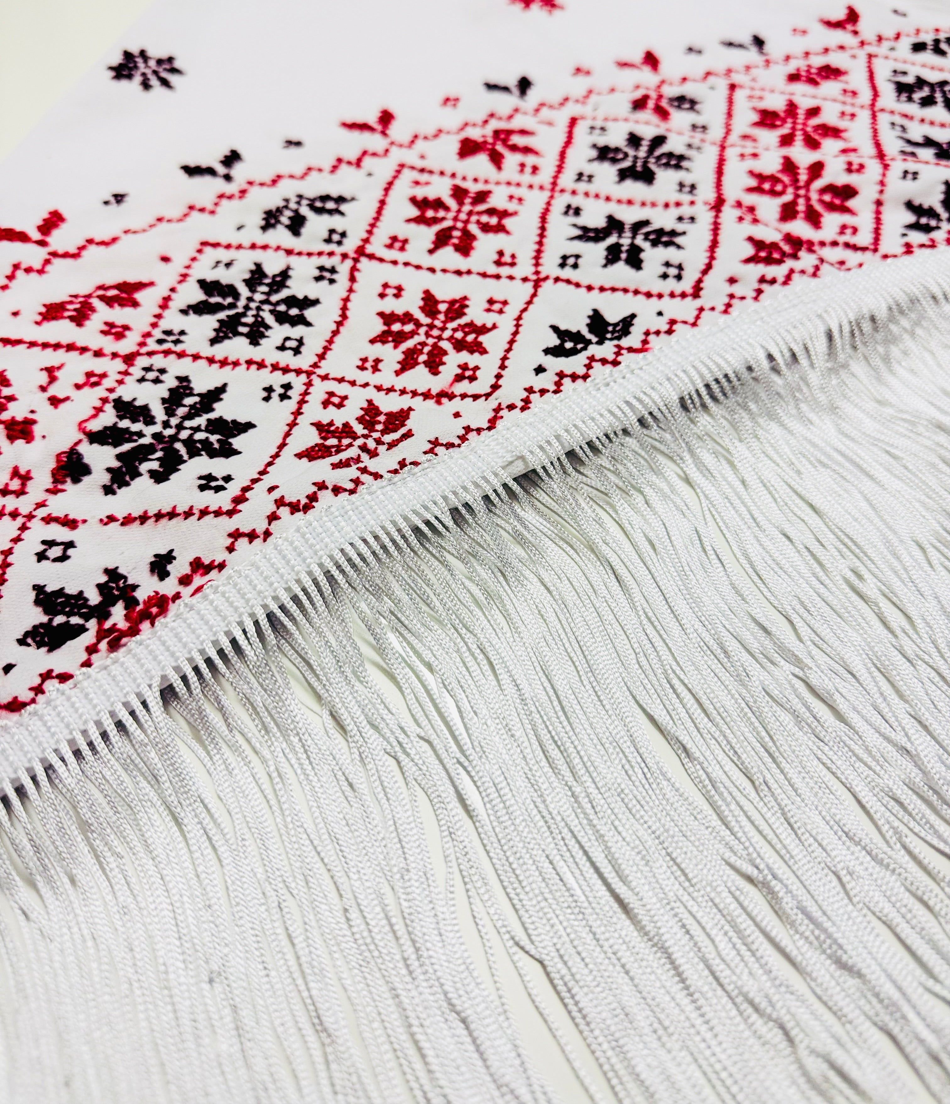 Nærbilde av hvitt tatreez-sjal med palestinsk broderimønster vist fra siden, detaljert skjerf inspirert av tradisjonelt tatreez-håndverk