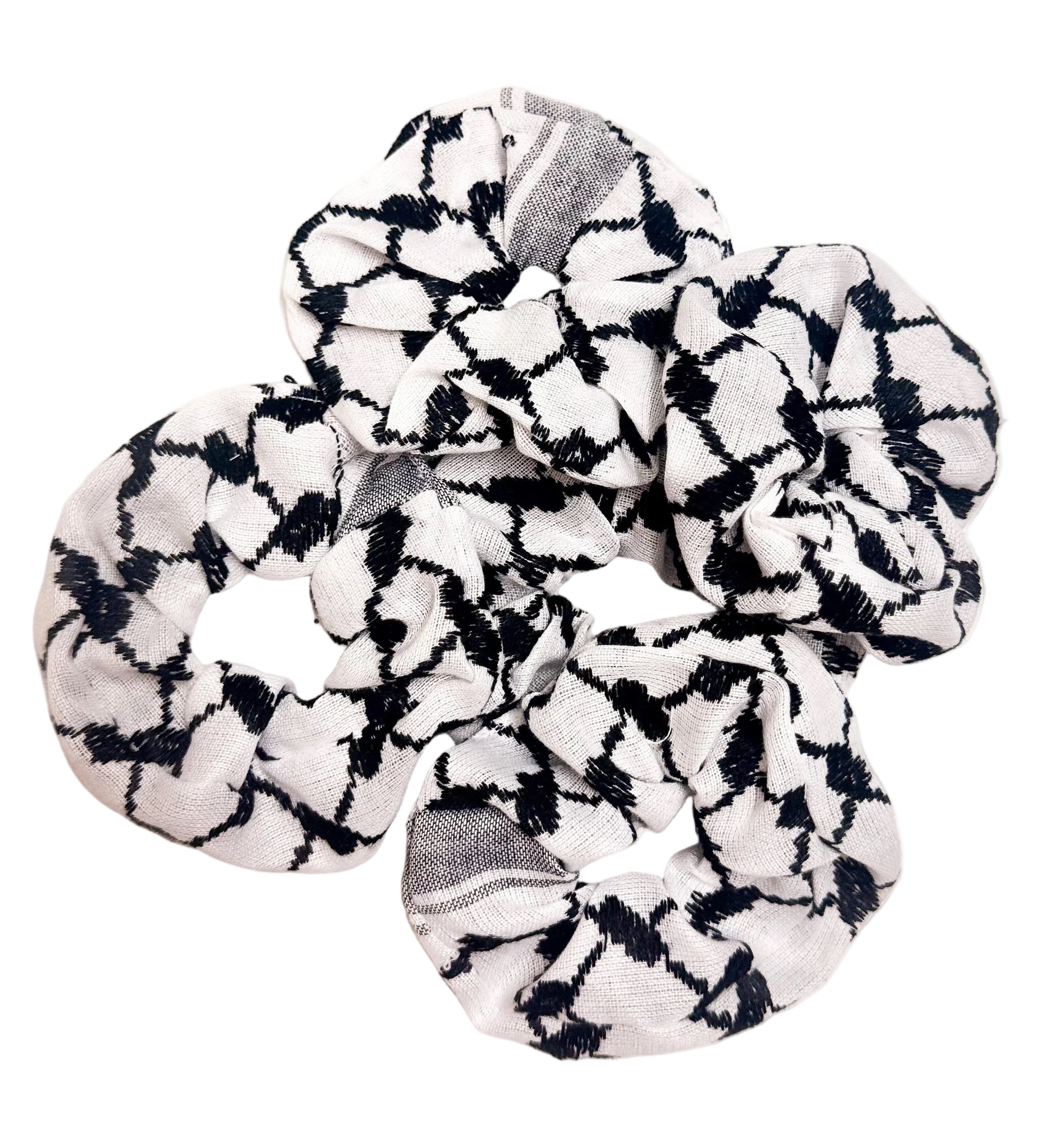 Flere svarte og hvite scrunchies med kufiyeh-mønster spredt på hvit bakgrunn, hårstrikker inspirert av tradisjonelt palestinsk design