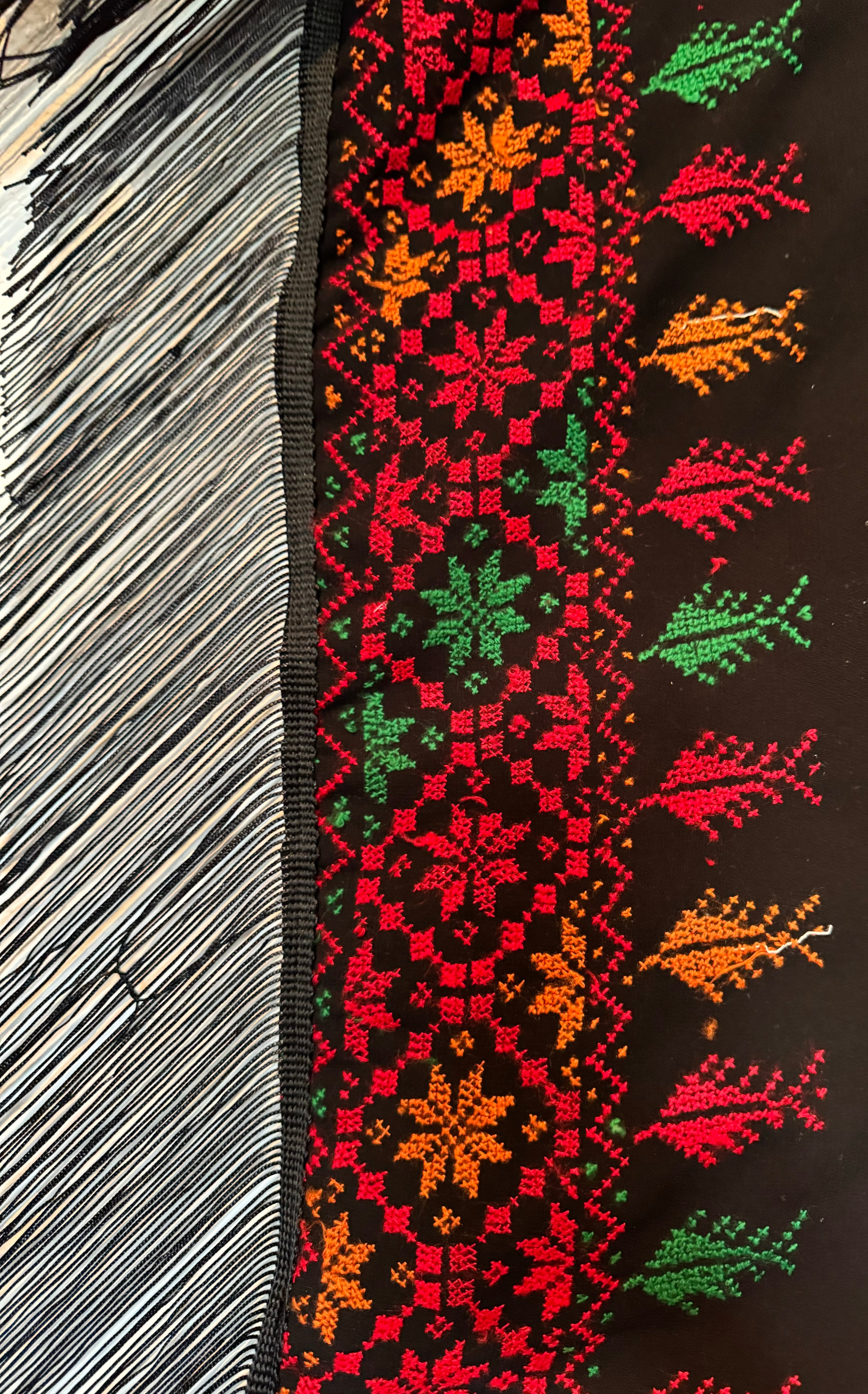 Tatreez-broderi langs kanten av et palestinsk skjerf, med geometriske mønstre i rødt, grønt og oransje.