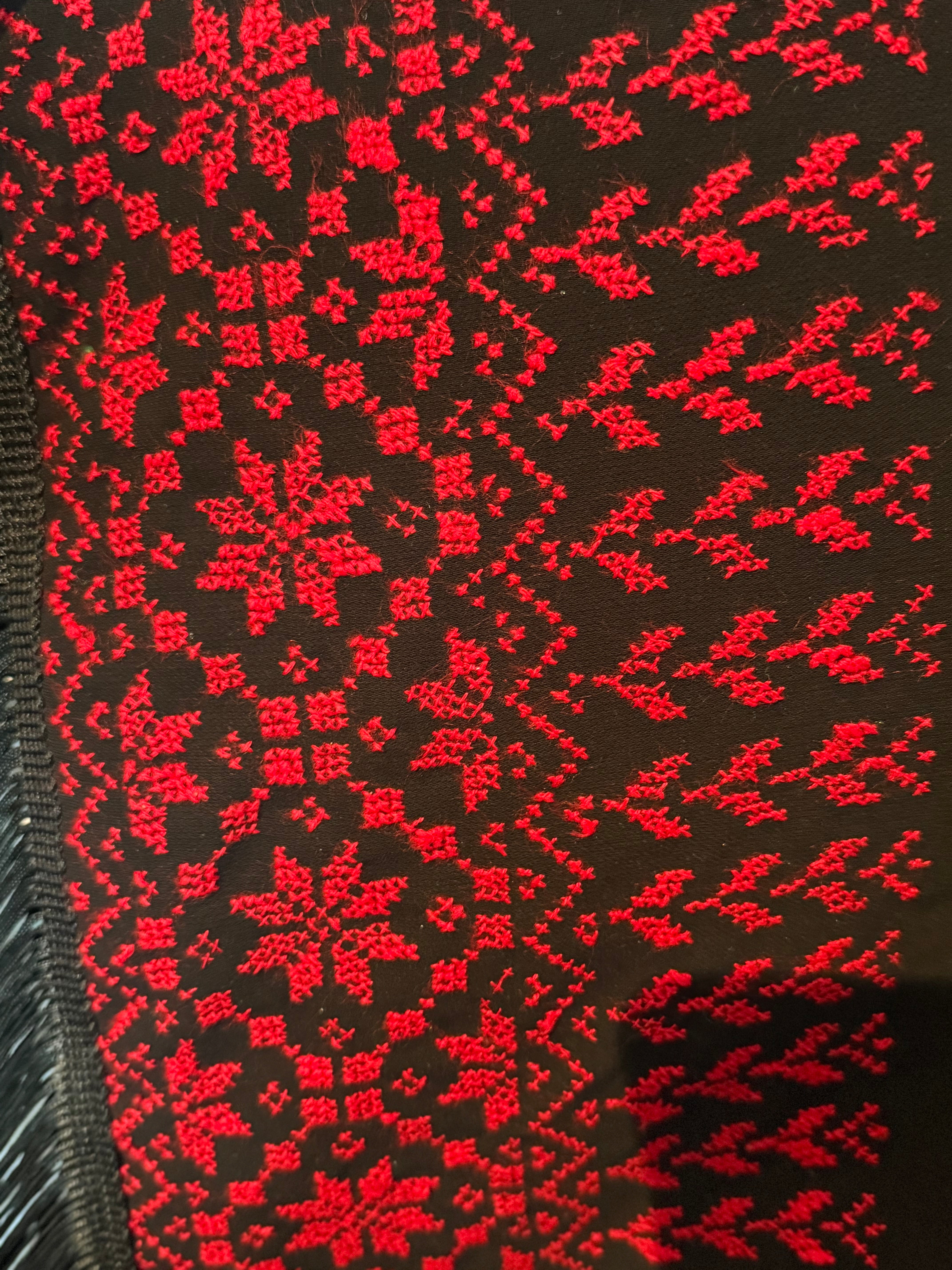 Tatreez-broderi i rødt på mørk bakgrunn, vist som detalj fra kanten av et palestinsk skjerf.