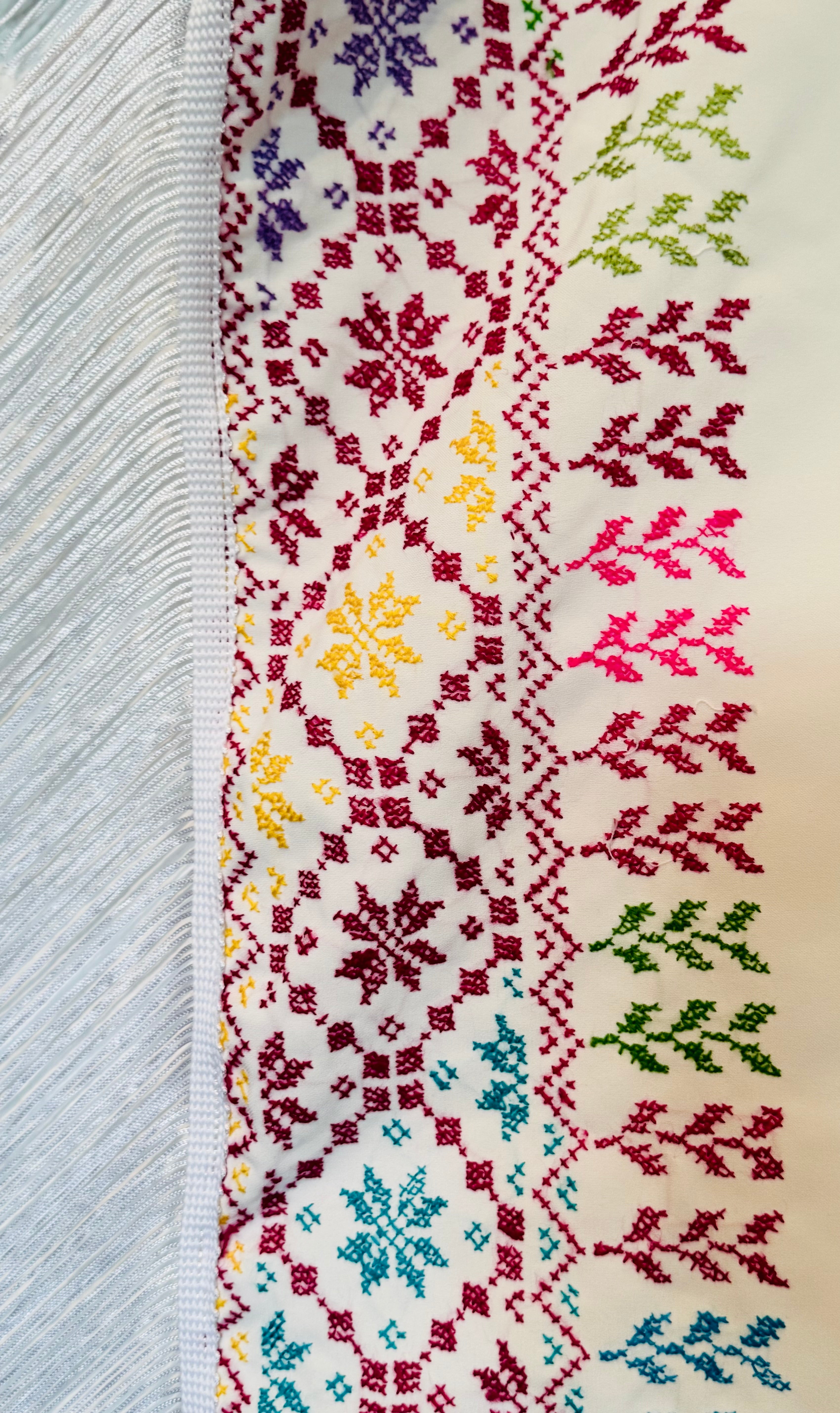 Nærbilde av hvitt tatreez-sjal med tydelig palestinsk broderimønster, tradisjonelt håndverk vist i tekstilstruktur