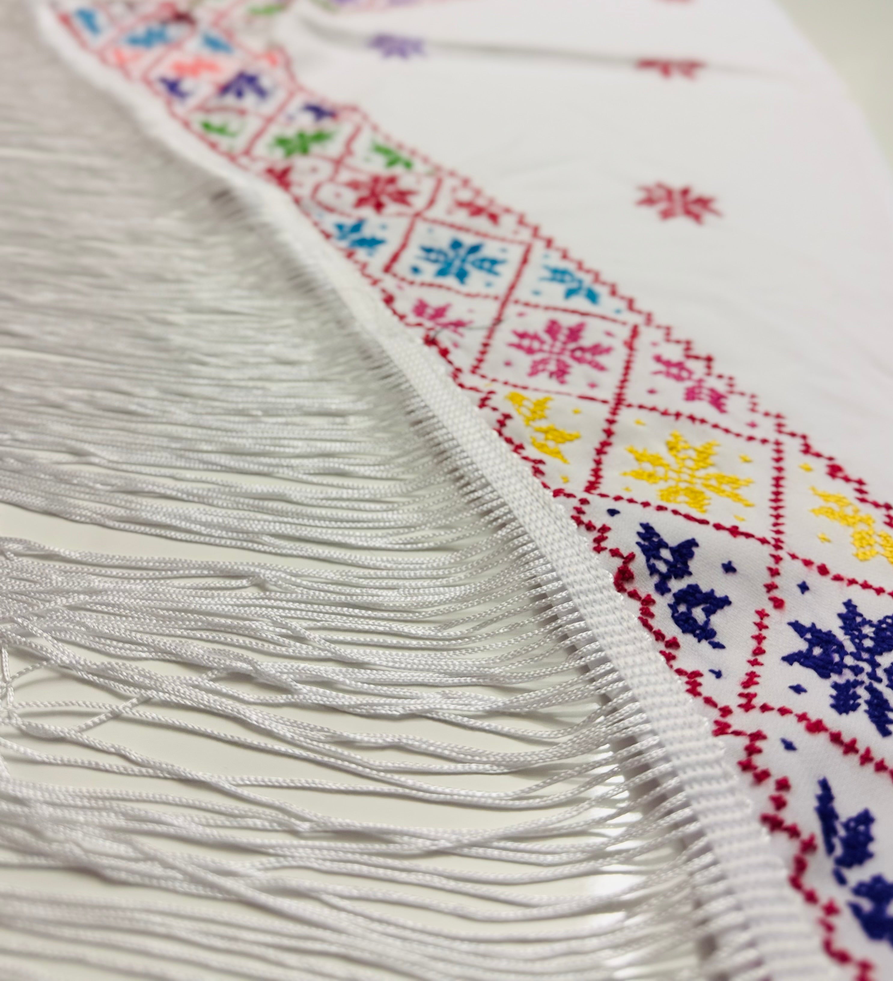 Detaljert nærbilde av hvitt tatreez-sjal med delikat palestinsk broderimønster, vist i annen vinkel for fremheving av tekstur