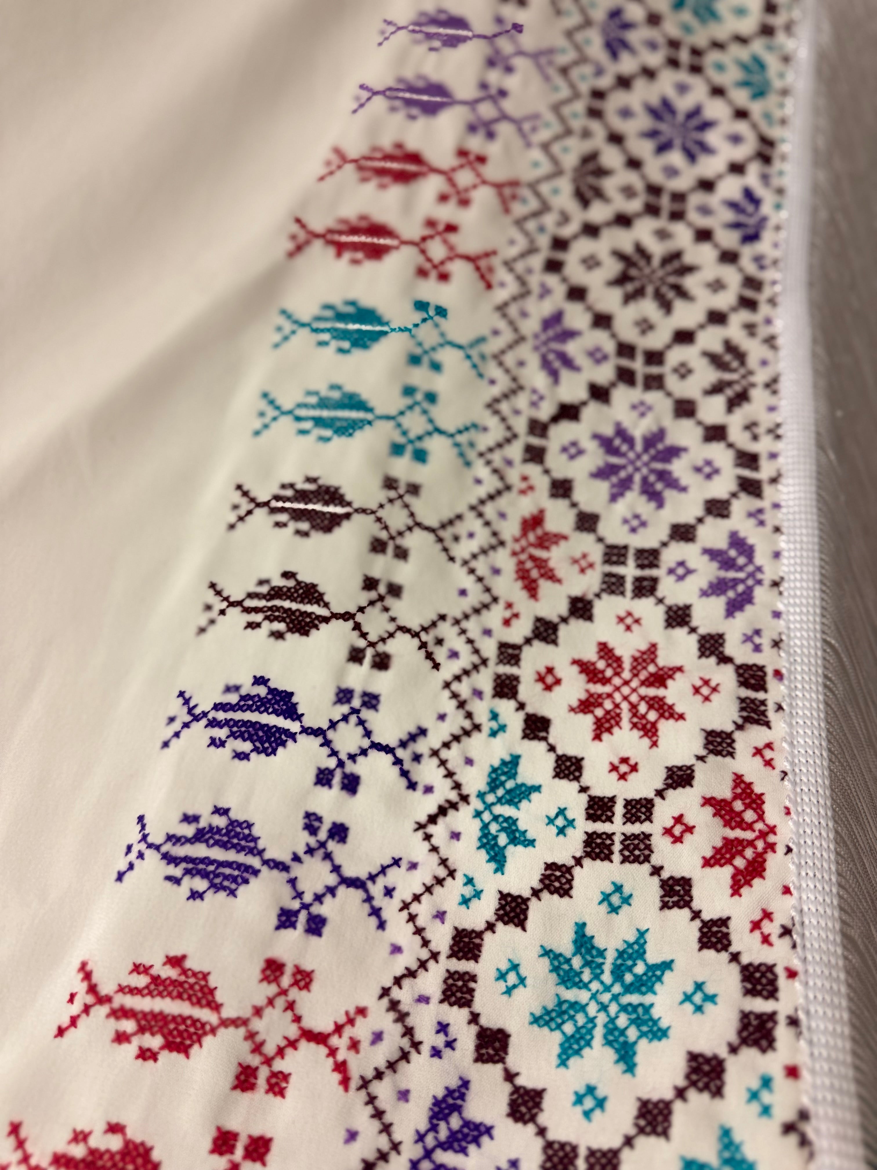 Vinkelbilde av hvitt tatreez-sjal med palestinsk broderimønster, tradisjonelt håndverk vist med tydelig tekstur