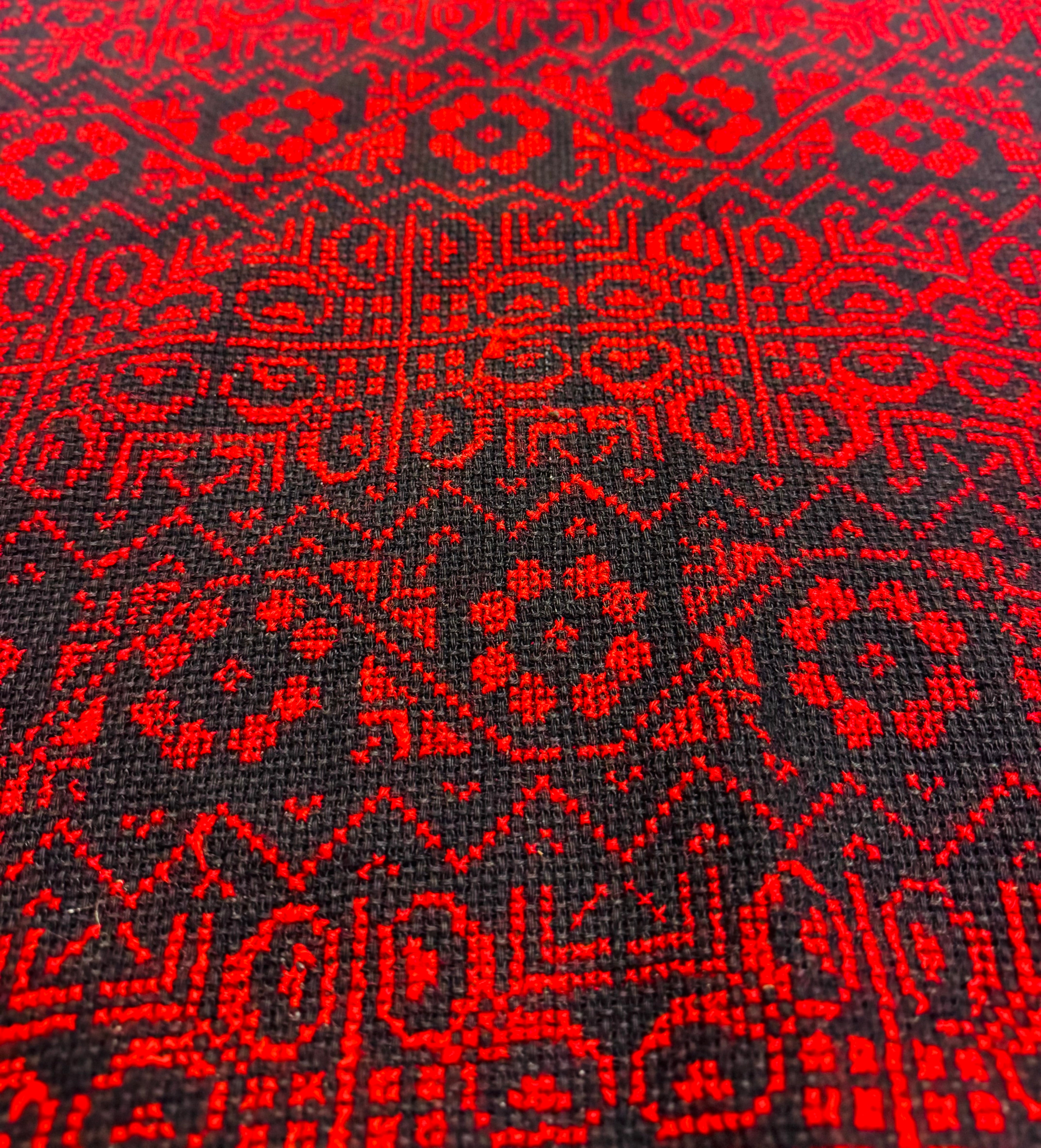 Skråbilde av rødt og svart palestinsk tatreez-broderi med geometriske mønstre, detaljert håndverk vist i tekstilstruktur