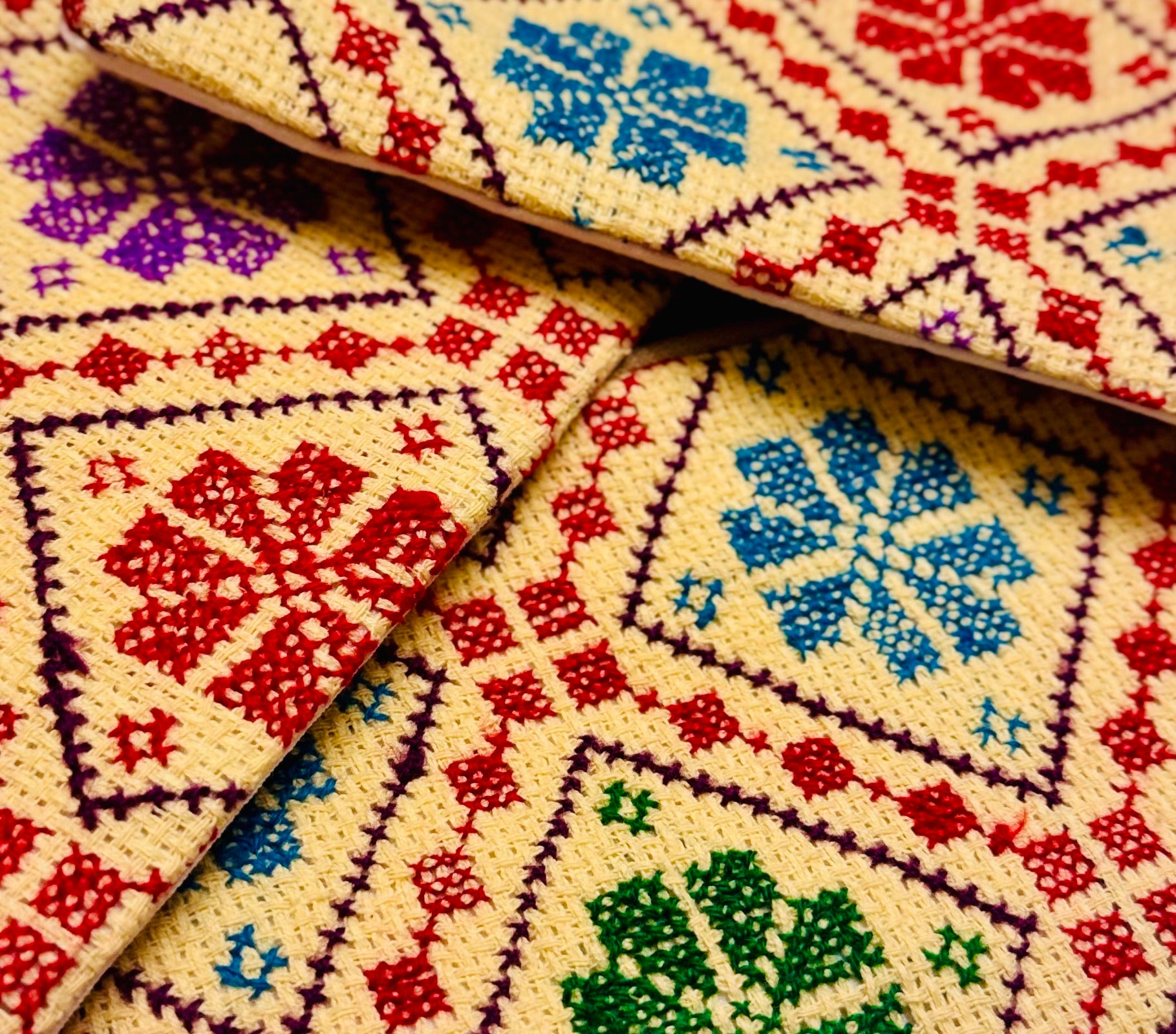 Nærbilde av broderiet på en beige tatreez-lommebok, der trådar og mønsterdetaljer kommer tydelig frem i tekstilet.