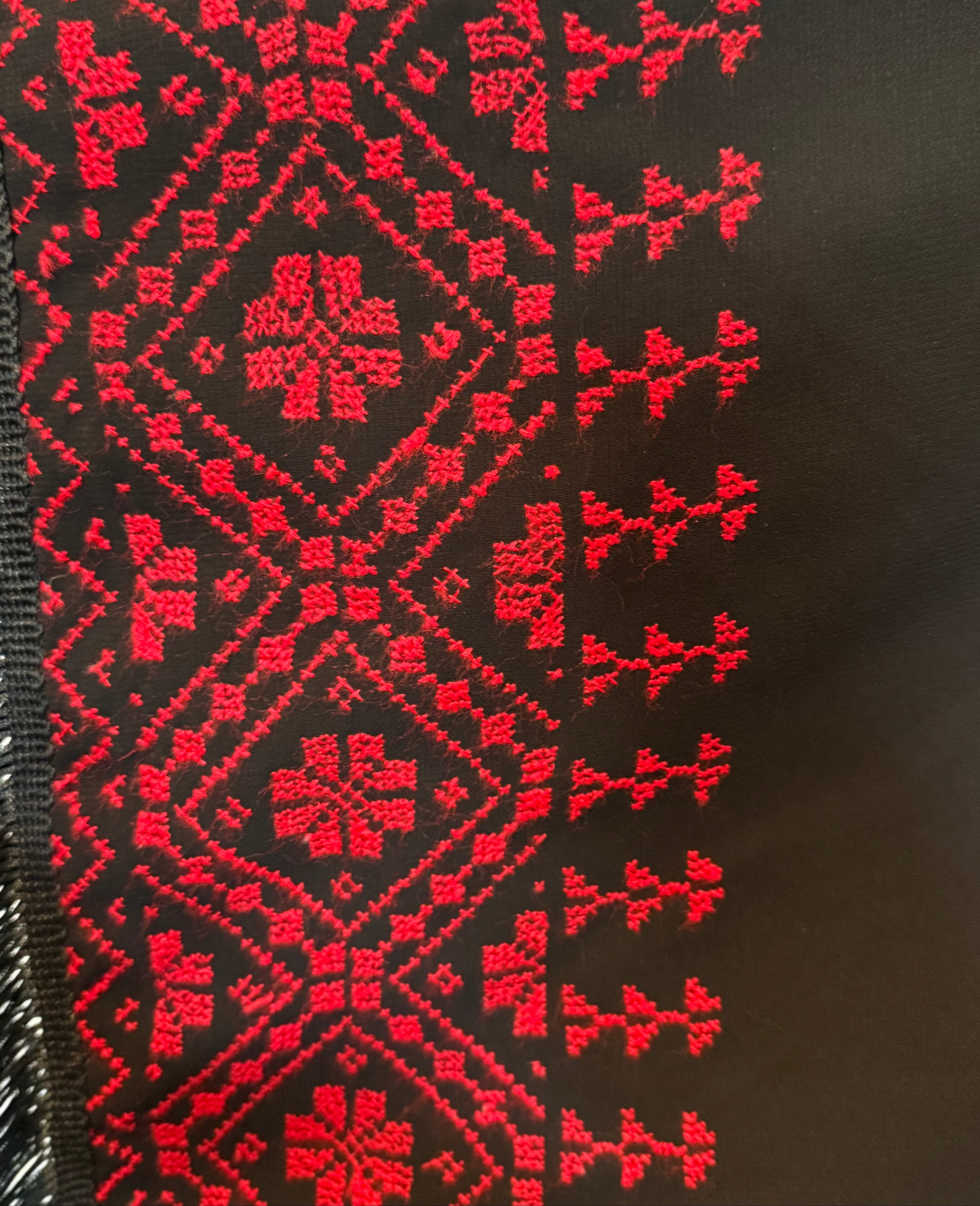 Rødt tatreez-broderi på mørkt skjerf, med markerte diagonale former og tett stingarbeid.
