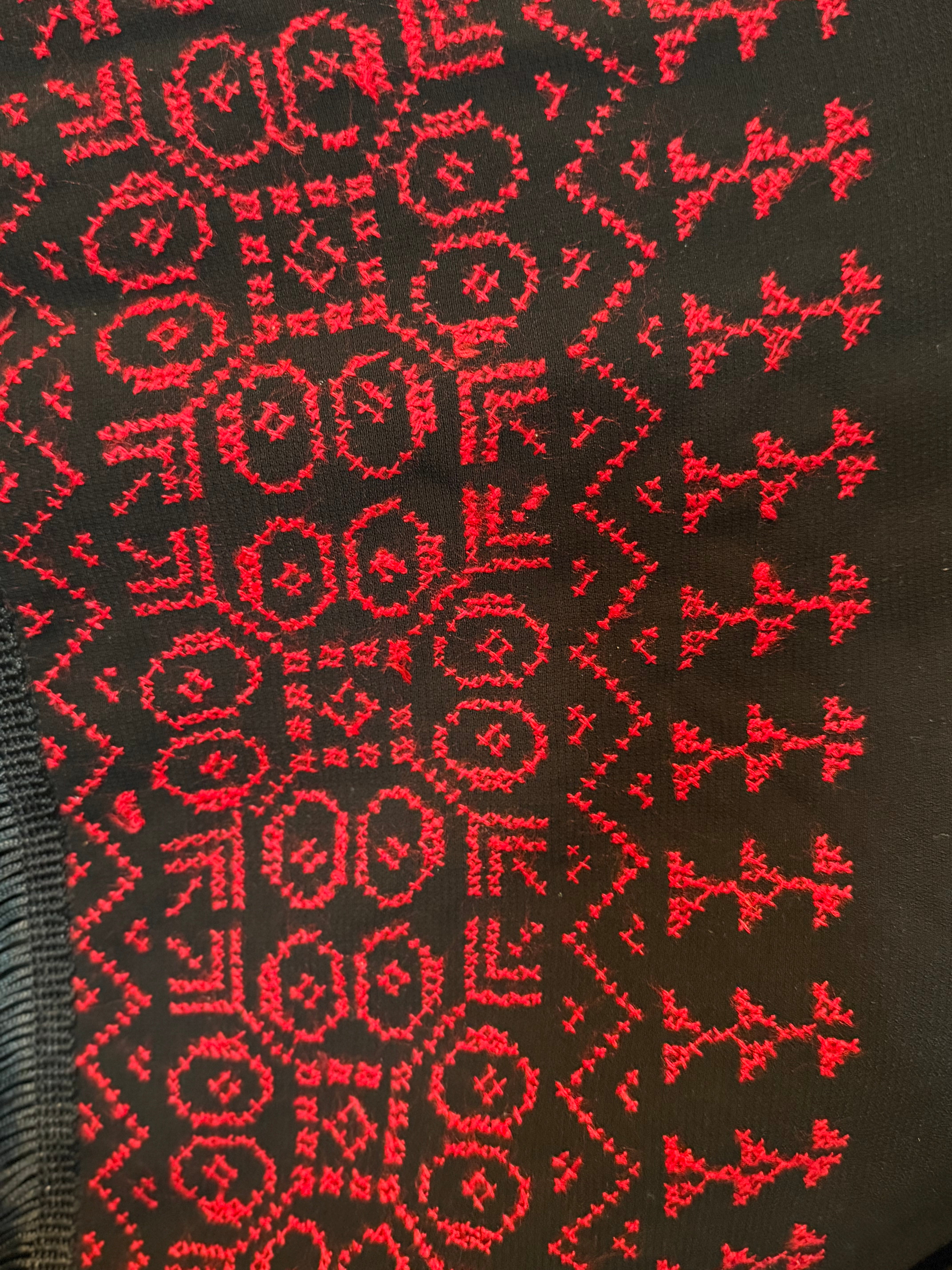 Nærbilde av rødt tatreez-mønster brodert på sjal, med tette geometriske figurer.