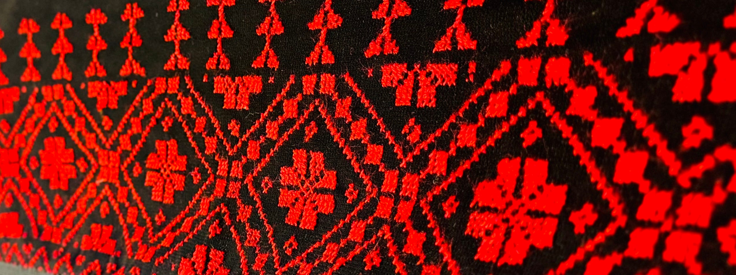 Horisontalt bilde av rødt og svart palestinsk tatreez-broderi med detaljerte geometriske mønstre i vevd tekstil