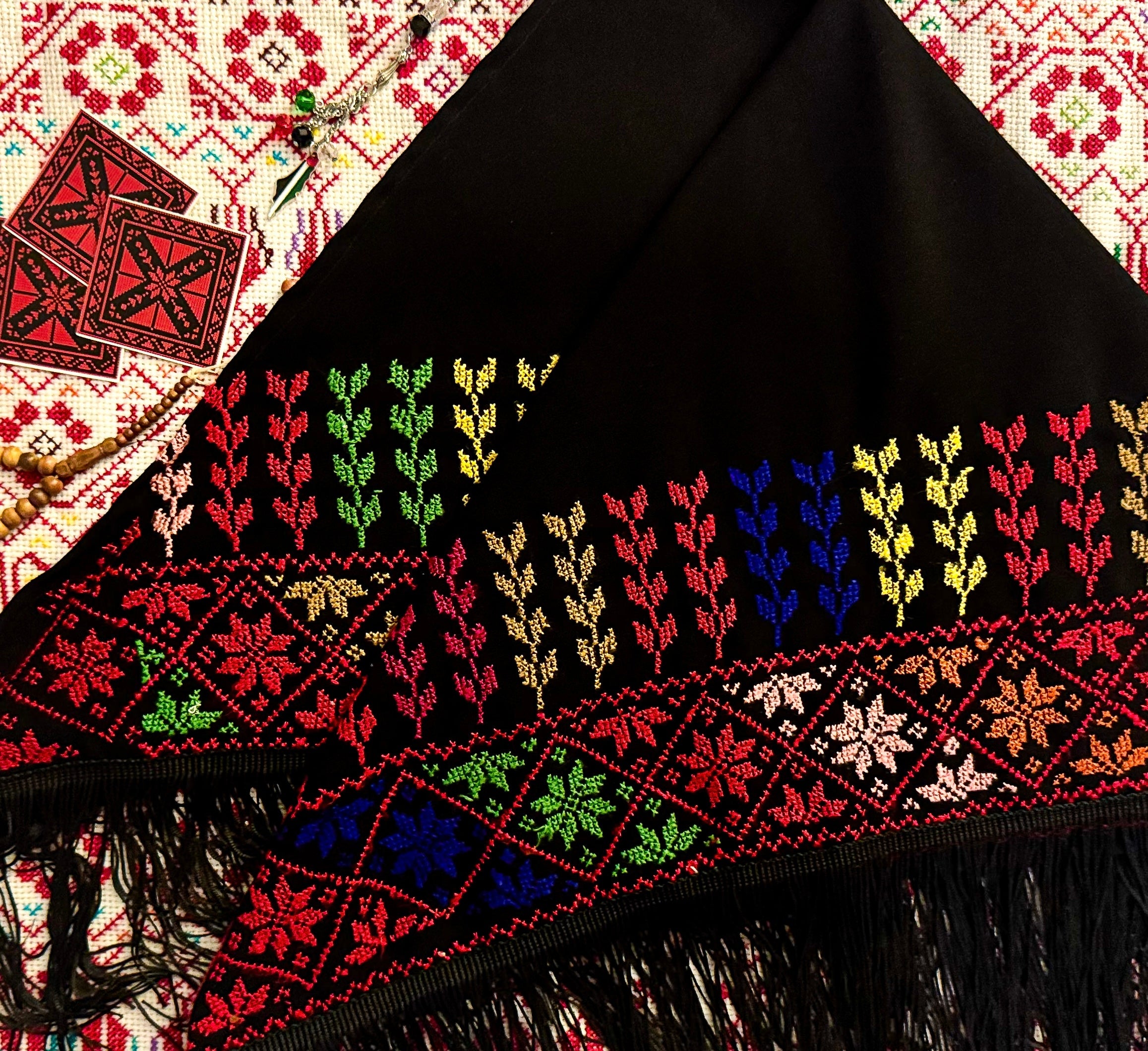 Tatreez-sjal med flerfarget palestinsk broderimønster, presentert mot bakgrunn av matchende tradisjonelt tatreez-tekstil