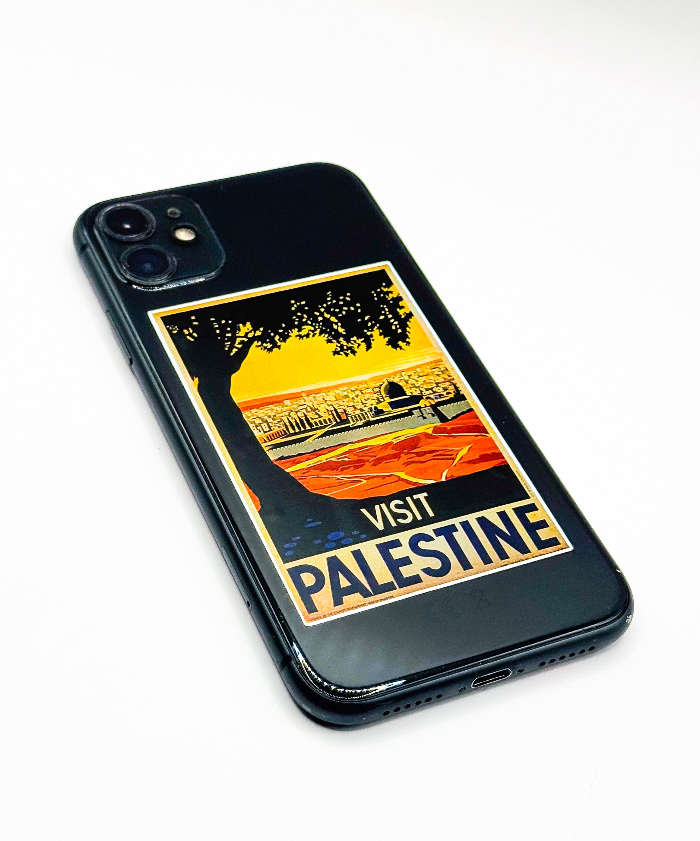 Mobiltelefon med «Visit Palestine»-klistremerke festet på baksiden, fotografert fra skrå vinkel.