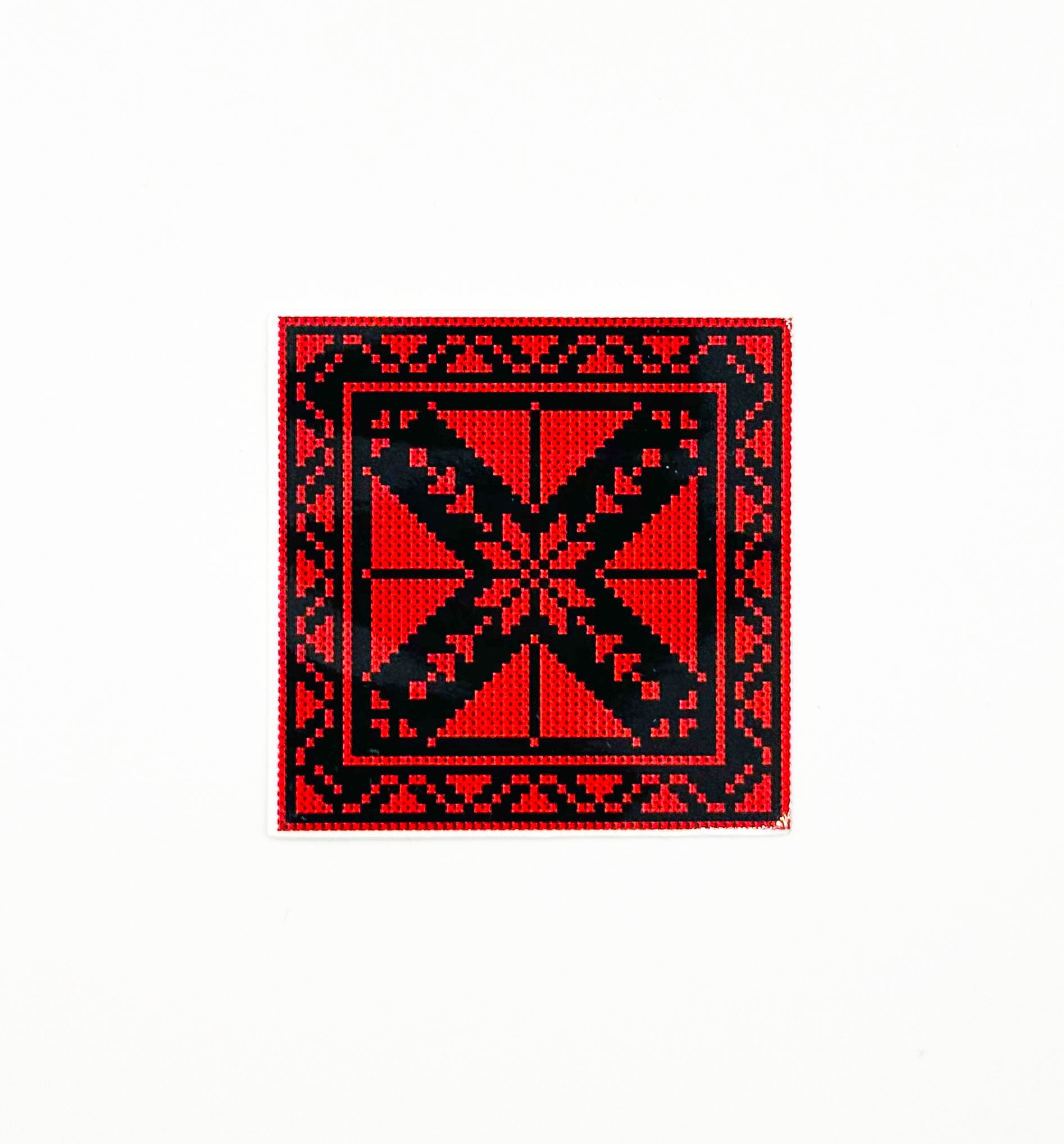 Rødt og svart tatreez-inspirert klistremerke med geometrisk broderimønster på kvadratisk flate.
