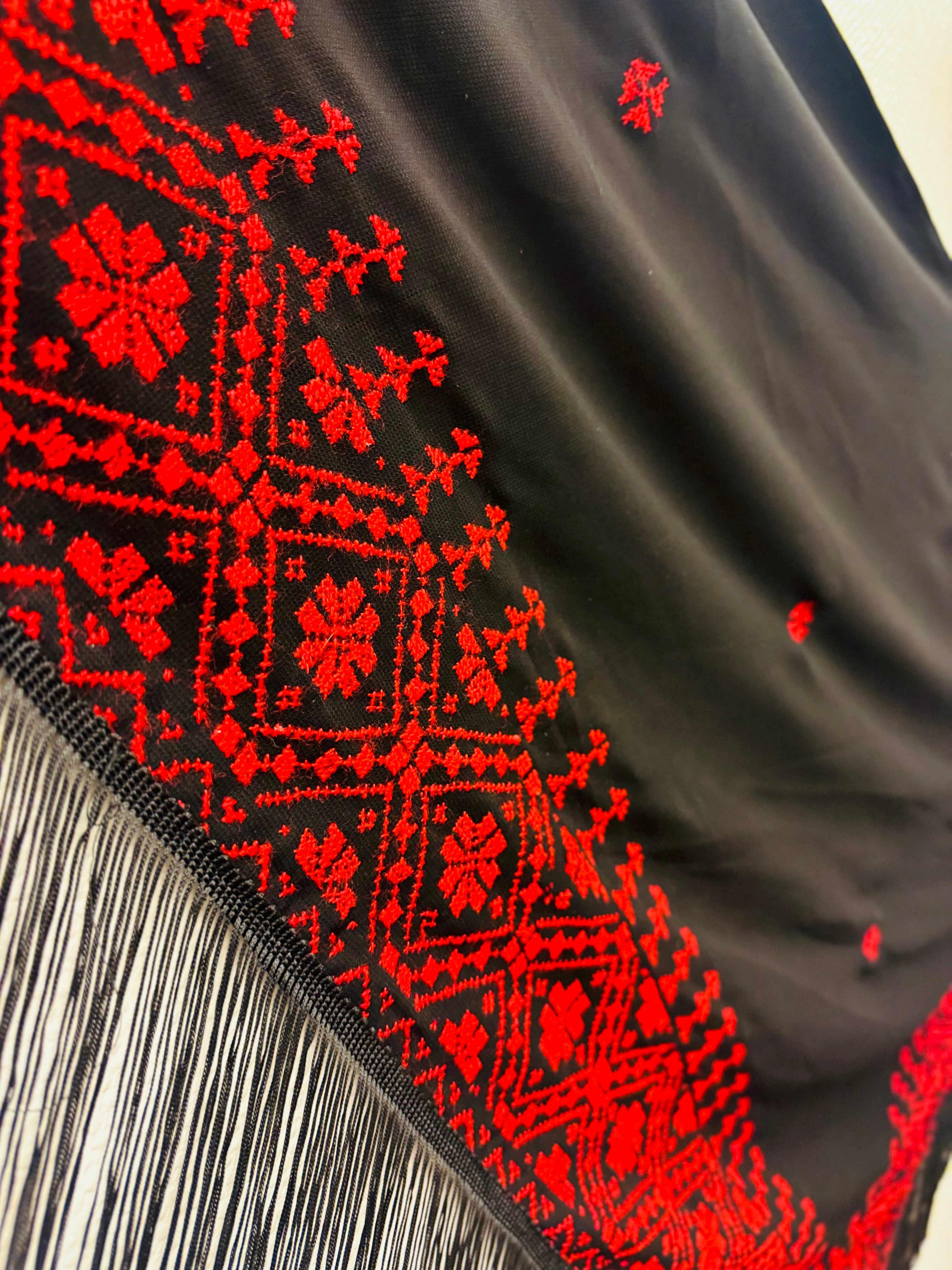 Vinkelbilde av rødt og svart tatreez-sjal med tydelig palestinsk broderimønster, tradisjonelt skjerf inspirert av klassisk tatreez-håndverk