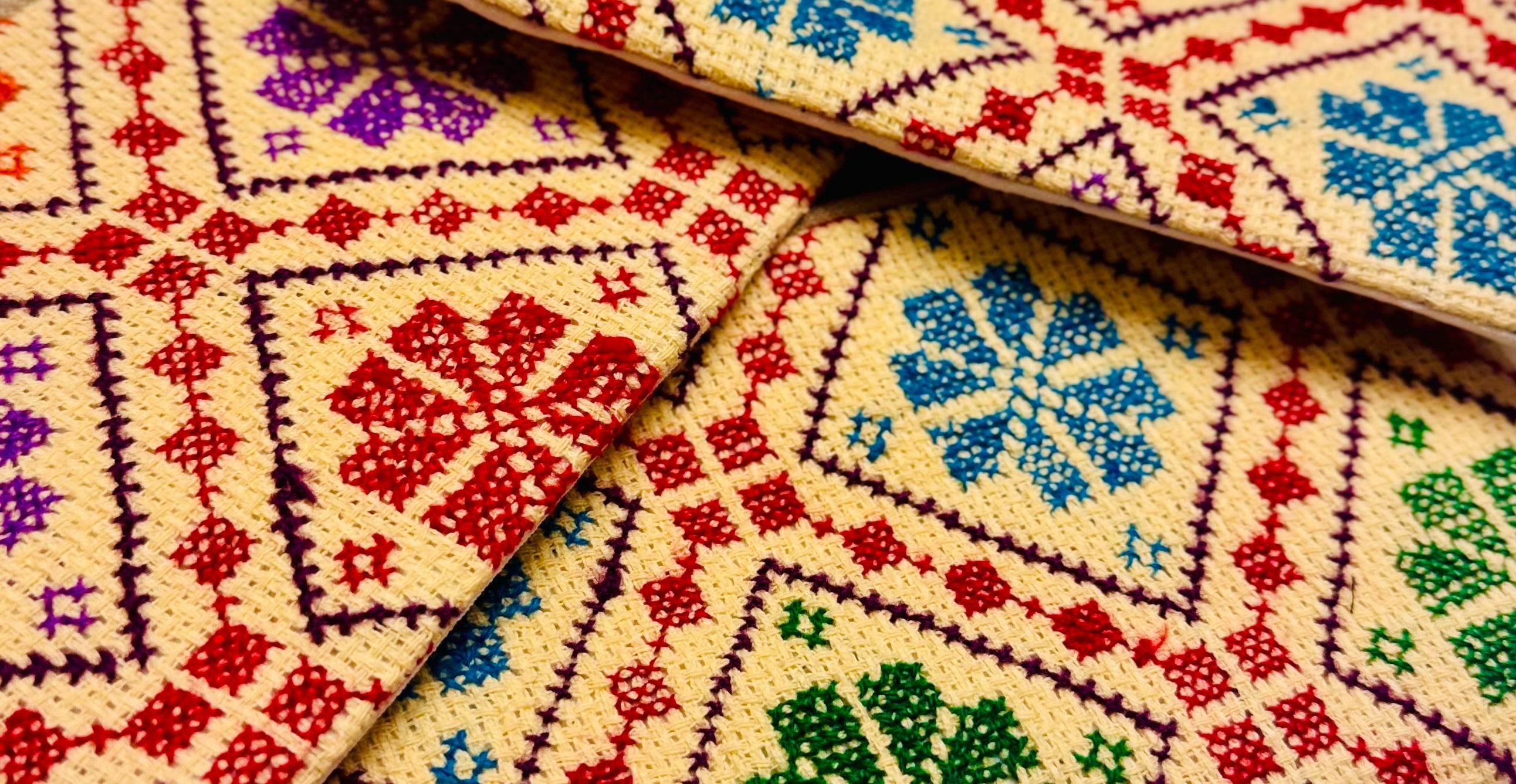 Horisontalt nærbilde av tatreez-broderi på beige lommebok, med fokus på mønsterets bredde og håndsydde detaljer.